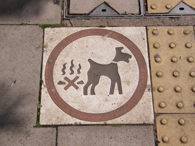 A pavement sign showing a dog and a pile of doggy do with a red cross through it